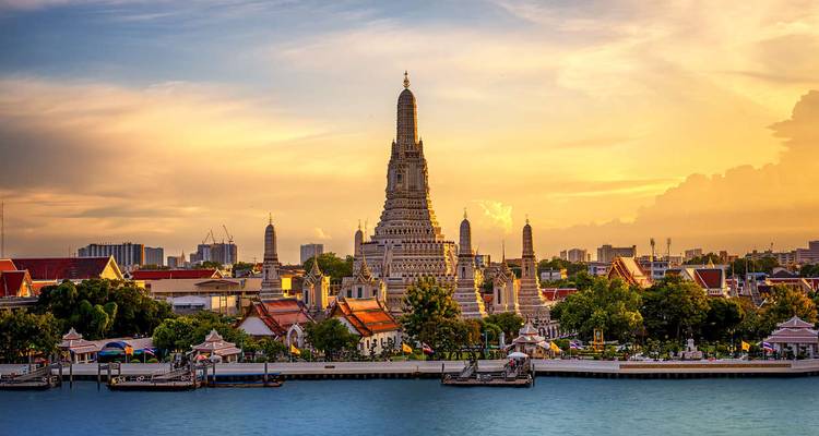 Wat Arun temple spires glow at sunset beside the Chao Phraya River.
