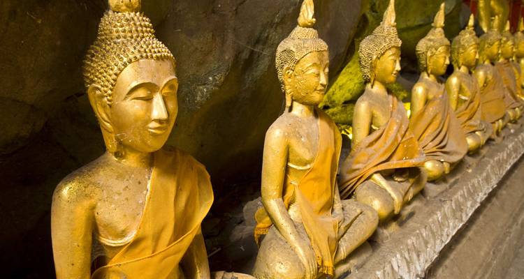 Row of golden Buddha statues in a dimly lit cave temple.