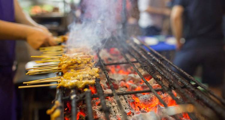 Skewers of meat grill over red-hot charcoal sending up aromatic smoke at a night market.