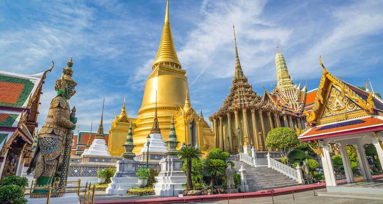 Grand Palace complex with gilded stupas and ornate temples glistens under a bright blue sky.