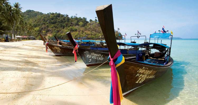 Colorful long-tail boats lined up on a white-sand beach with turquoise water in southern Thailand.