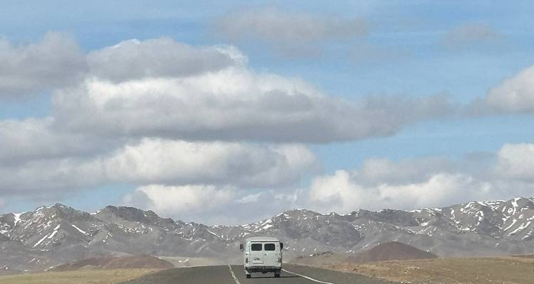 Una furgoneta solitaria conduciendo por una carretera rodeada de montañas.