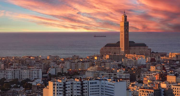 Paysage urbain au coucher du soleil avec une mosquée et l'océan en arrière-plan.