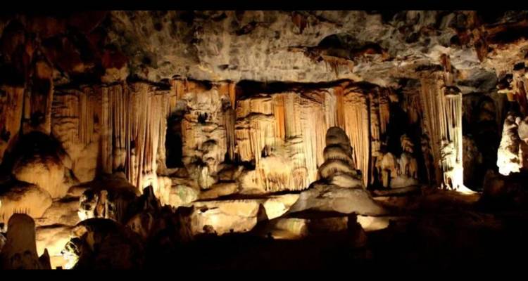 Interior of limestone cave with dramatic stalactites, stalagmites and warm artificial lighting.