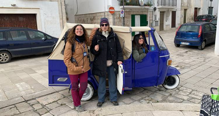 Trois voyageurs sourient à côté d'un tuk-tuk trois roues bleu éclatant sur une ruelle pavée.