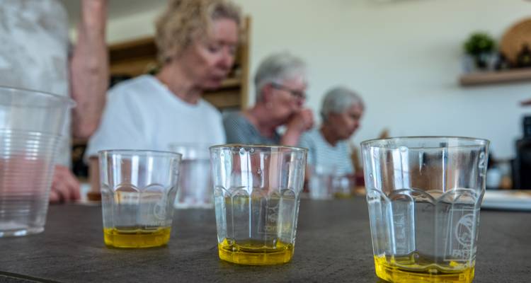 De petits verres d'huile d'olive dorée disposés pour la dégustation avec les participants en arrière-plan flou.