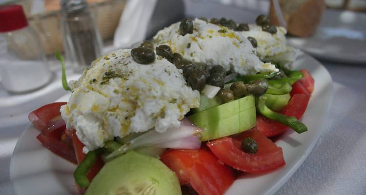 Salade grecque avec câpres et feta sur une assiette blanche.