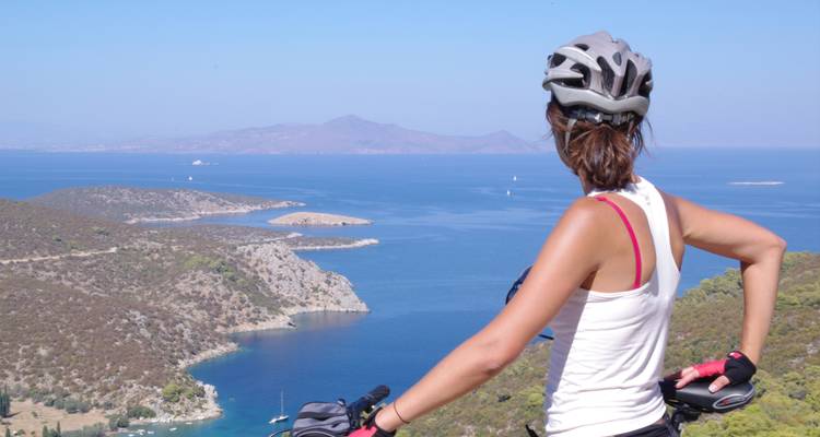 Femme à vélo surplombant la mer avec des îles en arrière-plan.