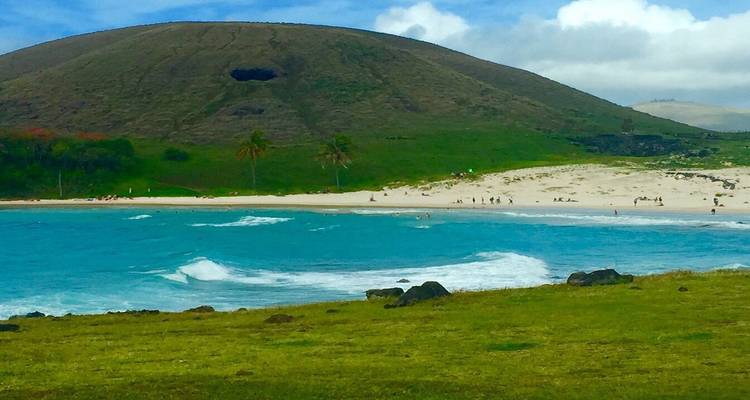 Eaux turquoise et une plage de sable avec une colline en arrière-plan.