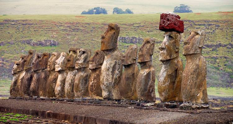 Rangée de statues Moaï avec une surmontée d'une pierre rouge.