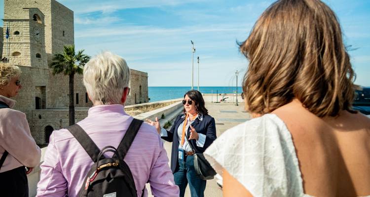 Le guide fait des gestes tout en expliquant l'histoire côtière près d'une tour en pierre et de la mer Adriatique.