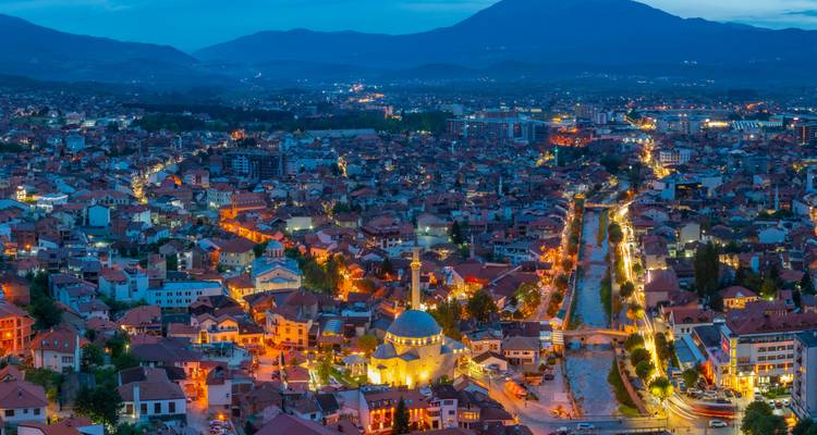 Paisaje urbano panorámico nocturno con edificios iluminados y un río serpenteante.