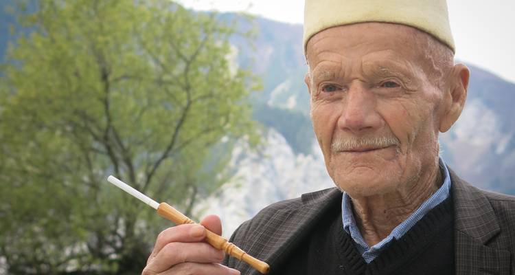 Hombre anciano sosteniendo una pipa de madera tradicional al aire libre.