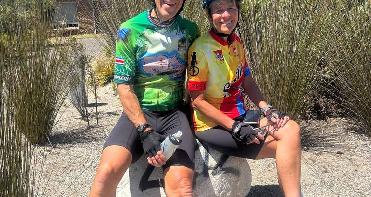 Deux cyclistes en maillots colorés se reposant sur un banc en pierre.