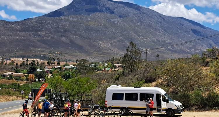 Groupe de cyclisme se regroupant près du véhicule d'assistance sous une imposante chaîne de montagnes.