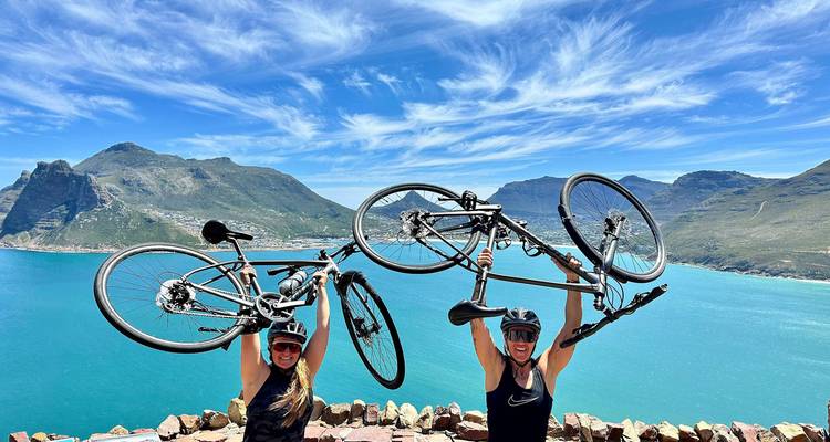 Deux cyclistes joyeux soulèvent leurs vélos au-dessus de leur tête surplombant la baie turquoise de Hout Bay.