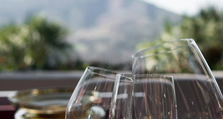 Gros plan de verres à vin élégants sur une terrasse avec des vignobles verts flous et des montagnes lointaines en arrière-plan.