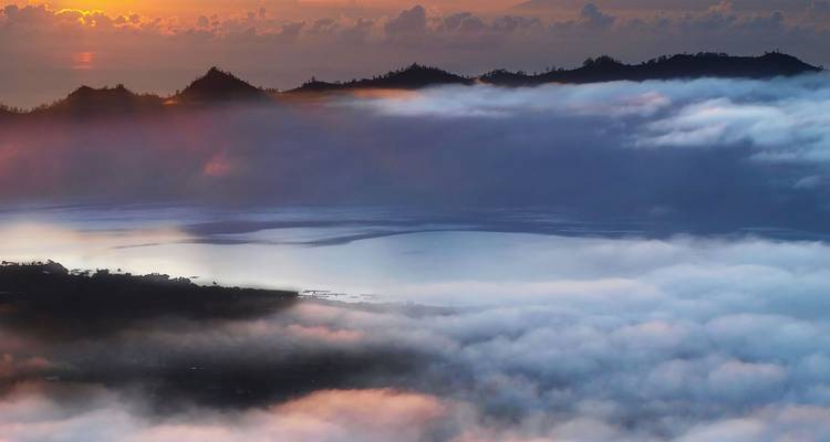 Vistas de un amanecer de ensueño sobre un mar de nubes llenando la caldera volcánica con picos silueteados y colores pastel cálidos.