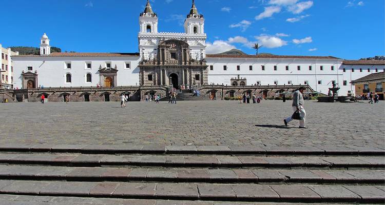 Ruim plein voor de witte San Francisco-kerk in Quito onder een strakblauwe hemel.
