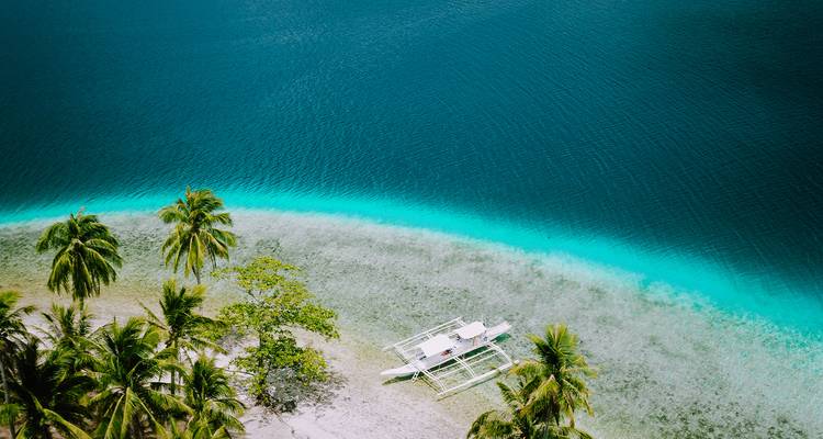 Banc de sable immaculé avec un petit bateau et des palmiers.