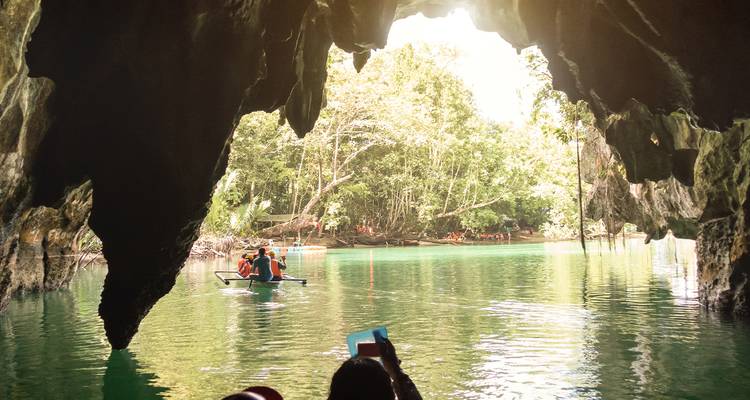 Un bateau à l'intérieur d'une ouverture de grotte donnant sur un paysage verdoyant luxuriant.