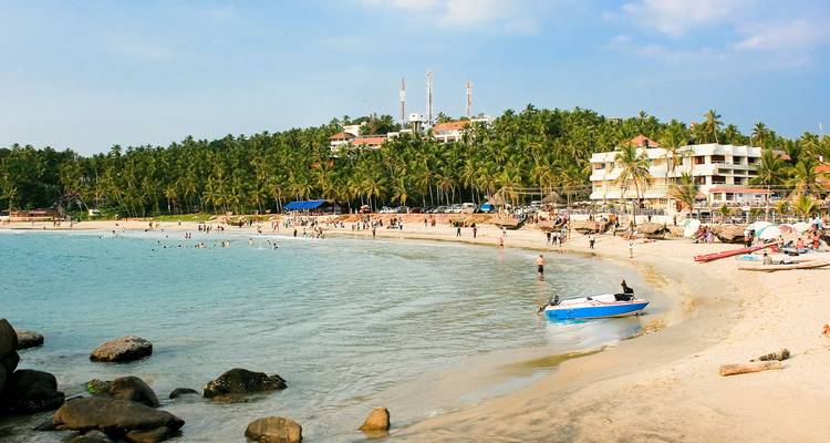 Les visiteurs nagent et se détendent le long de la rive sablonneuse et courbe de la plage de Kovalam, bordée de palmiers et de complexes hôteliers.
