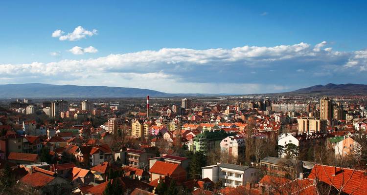 Vue panoramique sur la ville aux toits rouges de Niš entourée de collines lointaines sous un ciel bleu.