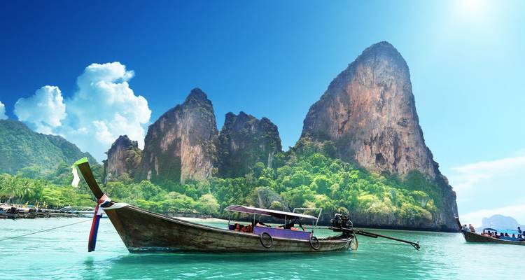 Bote de cola larga tradicional flotando en aguas cristalinas con acantilados de piedra caliza imponentes en Railay, Krabi.