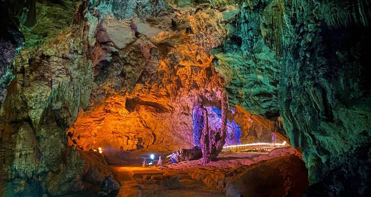 Interior de cueva coloridamente iluminado que presenta una variedad de formaciones rocosas.