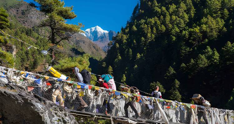 Des gens traversant un pont avec des drapeaux de prière dans une région montagneuse.