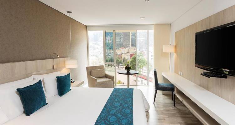 Modernes Hotelzimmer-Interieur mit einem Bett, Stühlen und Blick auf eine Stadt durch große Fenster.