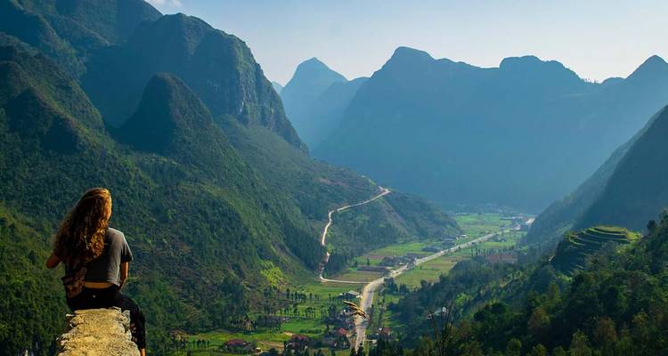 Persona sentada en el borde, admirando las amplias vistas del valle montañoso.