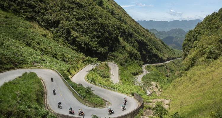Carretera serpenteante de montaña con motociclistas circulando a través de un paisaje exuberante.