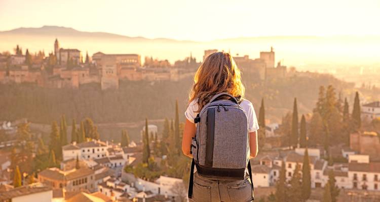 Person with a backpack overlooking a city at sunset.