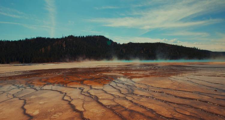 Hot spring with steam and colorful mineral patterns in Yellowstone.