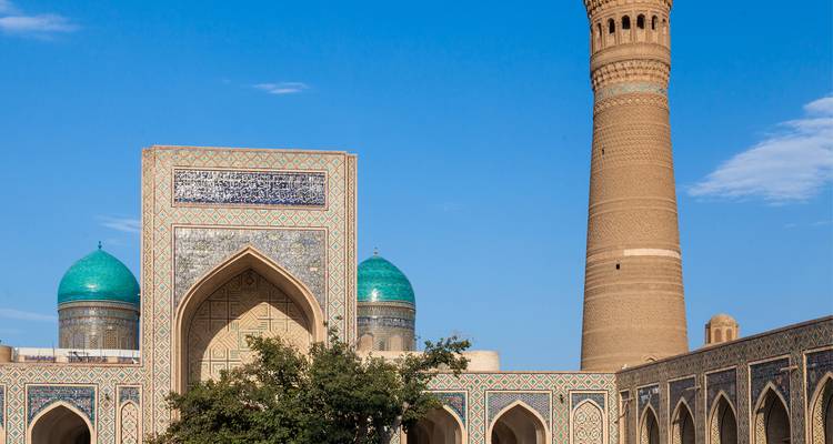 Madrasa ornée avec des dômes turquoise et un minaret élancé se détachant contre un ciel bleu clair en Ouzbékistan.