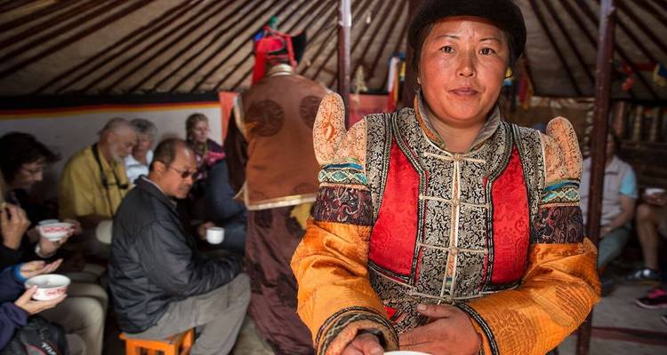 Mensen in een yurt die genieten van een maaltijd, met traditionele decoratie en kleding.