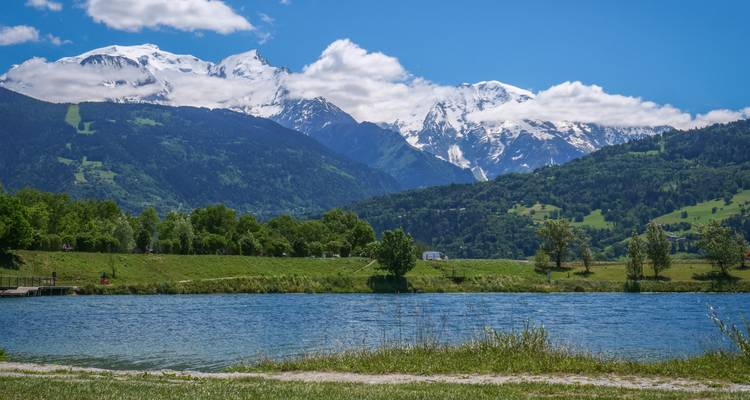 Macizo del Mont Blanc cubierto de nieve que se eleva sobre verdes valles y un tranquilo lago alpino.