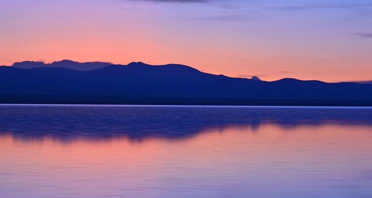 Silhouette of mountains with lake at sunset.