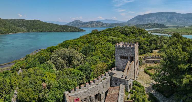 Ruinas del castillo con vista a un lago con colinas boscosas.
