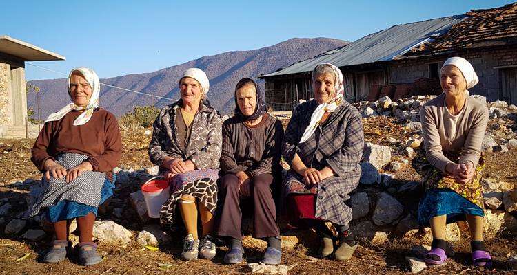 Grupo de mujeres sentadas en piedras con montañas de fondo.