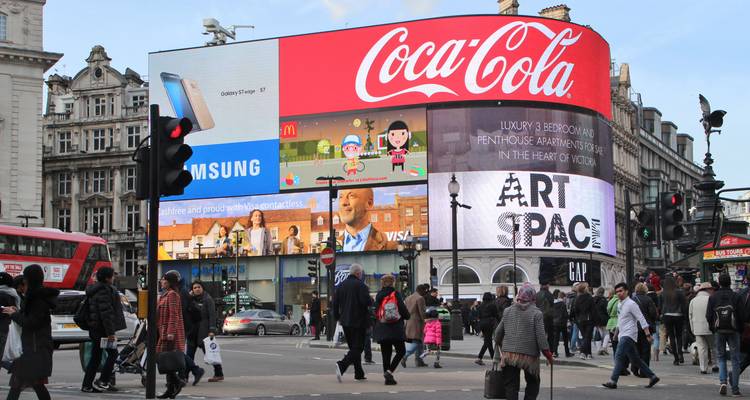 Busy Piccadilly Circus intersection with giant digital billboards and crowds crossing the street in central London.