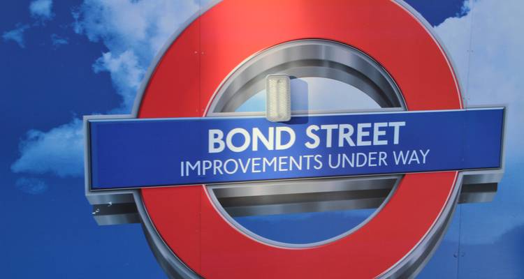London Underground roundel for Bond Street set against a bright blue hoarding announcing station improvements.