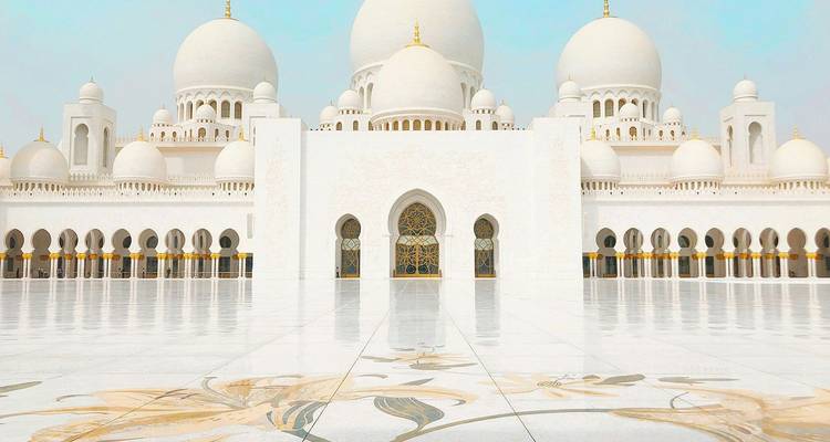 Symmetrisch vooraanzicht van de Sheikh Zayed Grote Moskee met bloemwerk ingelegd marmerplein.
