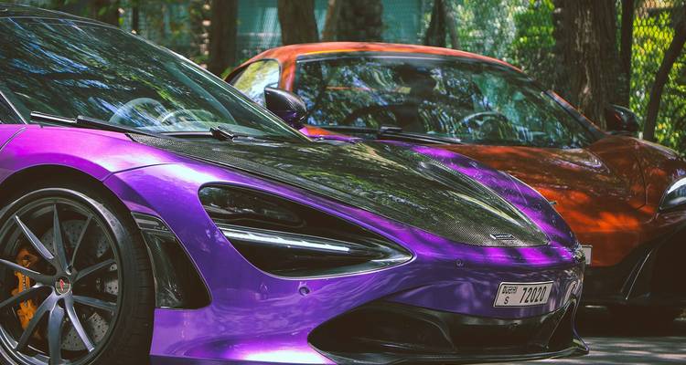 Glimmerende paarse en oranje supercars geparkeerd onder gevlekt schaduwlicht in een luxe stadse omgeving.
