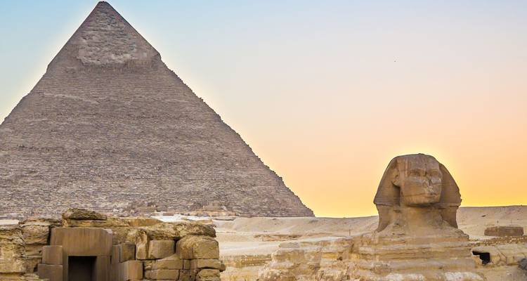 Esfinge recortada contra el cielo y la Gran Pirámide al atardecer con un cielo de puesta de sol pastel sobre el desierto
