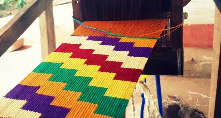 Colorful Kente cloth being woven on a traditional loom.