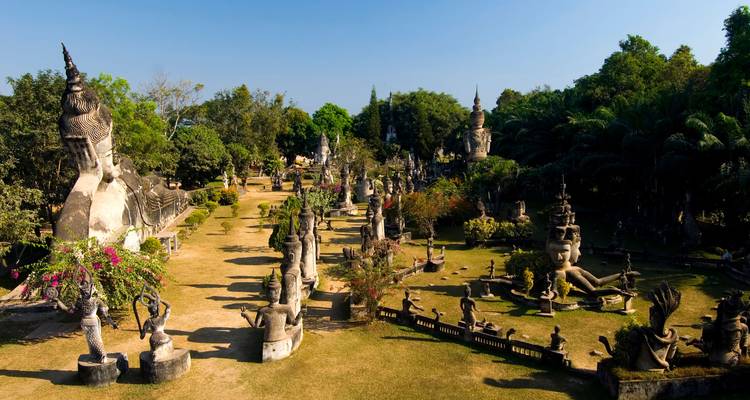 Expansive sculpture garden at Buddha Park with numerous concrete statues scattered among trees.