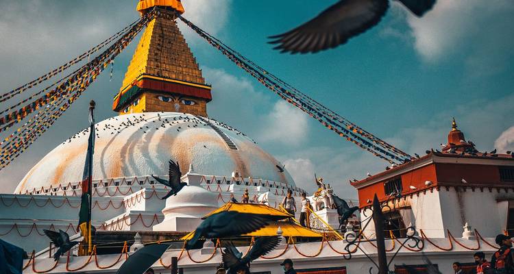 Boudhanath Stupa in Kathmandu with fluttering prayer flags and pigeons in flight.