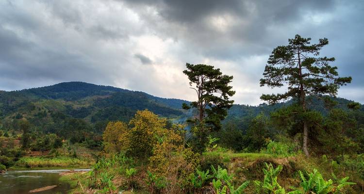 Paysage rural mouvementé de Madagascar avec des collines verdoyantes, une rivière et un ciel nuageux dramatique.